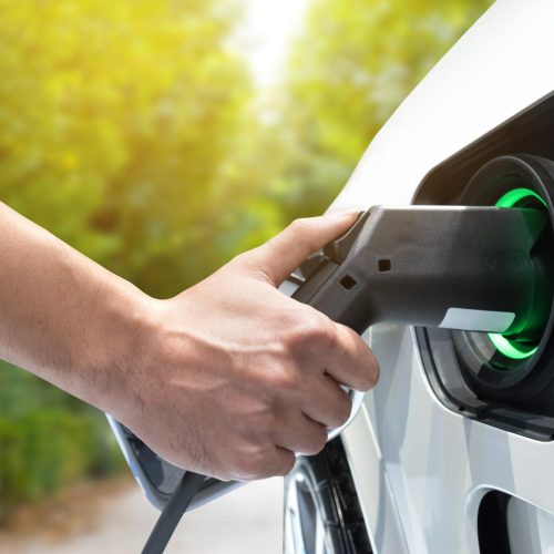 Electric vehicle charging station. Hand charging an electric car (EV) with the power cable supply plugged in.Flare light effect